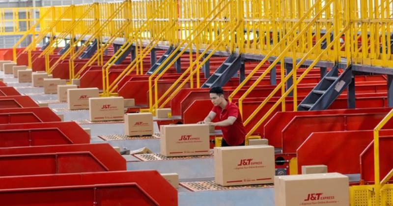 Hình ảnh một chiếc xe tải lớn đang vận chuyển hàng hóa, có logo hoặc biểu tượng gợi liên tưởng đến J&T Express hoặc hoạt động giao nhận bưu kiện.